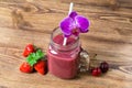 Healthy fruit smoothie with straw and orchid flower in a jar mug, with strawberries and cherries on a wooden background Royalty Free Stock Photo