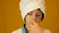 Healthy fruits and vitamins for children. Caucasian preschooler boy in cook uniform in a hat eats an apple. The child adores fruit