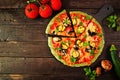 Healthy, gluten free green vegetable crust pizza with tomatoes, zucchini and mushrooms, table scene over dark wood