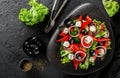 Healthy greek salad of fresh vegetables with tomatoes, lettuce, bell pepper, cucumbers, olives, feta cheese in plate on black Royalty Free Stock Photo