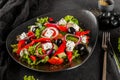 Healthy greek salad of fresh vegetables with tomatoes, lettuce, bell pepper, cucumbers, olives, feta cheese in plate on black Royalty Free Stock Photo