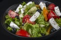 Healthy greek salad of fresh vegetables with tomatoes, lettuce, bell pepper, cucumbers, olives, feta cheese in plate on black ston Royalty Free Stock Photo