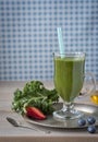 Healthy green smoothie with kale, strawberries, blueberries and honey in a glass against a rustic wood background.