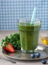 Healthy green smoothie with kale, strawberries, blueberries and honey on a vintage plate in a glass against a rustic wood backgrou