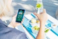 Healthy habit to drink water. Close up woman with glass bottle of pure water with lemon checking phone while sitting at