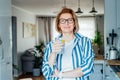 Healthy habit to drink water. Smiling middle age woman with glass of pure water with lemon standing on her kitchen