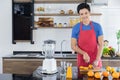 Healthy handsome man with casual clothes is smiling and preparing orange juice to diet, in kitchen at home in holiday Royalty Free Stock Photo