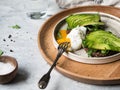Healthy homemade toasts with arugula and avocado on rye grain bread and poached egg with spreading yolk on plate on grey