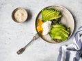 Healthy homemade toasts with arugula and avocado on rye grain bread and poached egg with spreading yolk on plate on grey