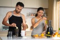 Healthy Indian couple preparing fruit juice and protein shakes after working out at kitchen - concept of active