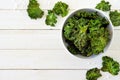 Healthy kale chips in a bowl, above scene on white wood with copy space.