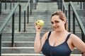 Healthy life. Positive plus size woman in sport clothing holding green apple and smiling while standing on stairs