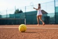 Healthy lifectyle. A young girl plays tennis on the court. The view on the ball and a tennis player. Dirt court.