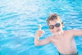 Healthy lifestyle. Active, happy nine years old child boy in sport goggles showing thumbs up on the swimming pool. Copy space.