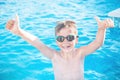 Healthy lifestyle. Active, happy nine years old child boy in sport goggles showing thumbs up on the swimming pool background.