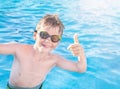 Healthy lifestyle. Active, happy nine years old child boy in sport goggles showing thumbs up on the swimming pool background.