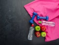 colored Apples dumbbells sport water bottles and purple towel on black concrete background