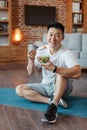 Healthy lifestyle concept. Happy middle aged asian man eating vegetable salad, sitting on yoga mat and smiling at camera Royalty Free Stock Photo