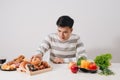 Healthy lifestyle concept - smiling young man comparing healthy and unhealthy food. fresh vegetables and hamburger Royalty Free Stock Photo