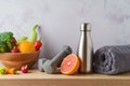 Healthy lifestyle and fitness concept. Bottle of water, dumbbells; towel, fruits and vegetables on wooden table over modern