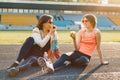 Healthy lifestyle and healthy food concept. Smiling fitness mother and teen daughter together eating apple sitting on stadium