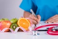 Healthy lifestyle, food and nutrition concept. Close up doctor woman hand holding pen to checklist with fresh vegetables and Royalty Free Stock Photo
