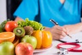 Healthy lifestyle, food and nutrition concept. Close up of fresh vegetables and fruits with stethoscope lying on doctor`s desk Royalty Free Stock Photo