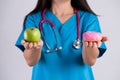 Healthy lifestyle, food and sport concept. Healthy versus unhealthy. Doctor woman hand holding donut and green apple