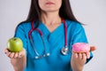 Healthy lifestyle, food and sport concept. Healthy versus unhealthy. Doctor woman hand holding donut and green apple