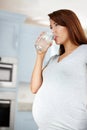 Healthy lifestyle means a healthy baby. Young pregnant woman drinking a glass of water in her kitchen. Royalty Free Stock Photo