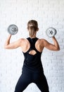 Rear view of an athletic woman in black sportwear showing her back and arms muscles training with a dumbbell Royalty Free Stock Photo