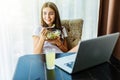 Healthy looking cheerful woman eating homemade organic fruit mix fruit salad while use laptop at home Royalty Free Stock Photo