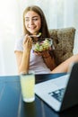 Healthy looking cheerful woman eating homemade organic fruit mix fruit salad while use laptop at home Royalty Free Stock Photo