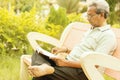 Healthy looking senior man in late 70s sitting in garden at home and reading book, outdoor - old man relaxing at Park by seriously Royalty Free Stock Photo