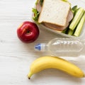 Healthy lunch box with sandwich, fruits and bottle of water on white wooden surface, top view. From above, flat, overhead