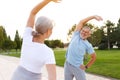 shot of happy smiling mature family man and woman in sportswear stretching arms while warming up together outdoors in park on sun Royalty Free Stock Photo