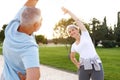 Full length shot of happy smiling mature family man and woman in sportswear stretching arms while warming up together outdoors in Royalty Free Stock Photo