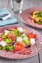 Healthy mixed Greek salad served on a pink plate with silver fork containing crisp leafy greens, microgreen, feta, onion Royalty Free Stock Photo