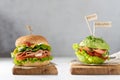 Healthy nutrition concept. Healthy raw avocado burger with salted salmon, fresh vegetables and microgreen and junk food burger Royalty Free Stock Photo