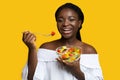 Healthy Nutrition. Happy black woman eating fresh vegetable salad over yellow background Royalty Free Stock Photo