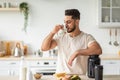 Athletic young Arab man drinking protein shake or milk, standing near table with healthy products at kitchen Royalty Free Stock Photo