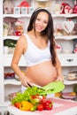 Healthy nutrition and pregnancy. Young smiling pregnant woman cuts vegetables on salad