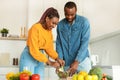 Healthy nutrition. Young african american couple cooking fresh vegetable salad in kitchen together Royalty Free Stock Photo