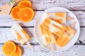 Healthy orange yogurt ice pops on a plate, top view against white wood