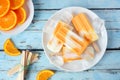 Healthy orange yogurt popsicles, top view table scene against blue wood