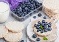 Healthy organic rice cakes with ricotta and fresh blueberries and glass of milk on light stone kitchen background. Top view. Plast