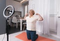 a healthy pensioner sits on the bedroom floor in front of a tripod for a camera, shoots a fitness video tutorial for the