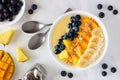 Healthy pineapple, mango smoothie bowl with coconut, bananas, blueberries and granola. Top view scene on a bright background.