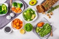 Healthy plant based food lunch, top view. Green salad, sweet potato, vegan cake, vegetables on white background Royalty Free Stock Photo