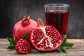 Pomegranate drink in a transparent glass near ripe open pomegranate fruits on a dark background